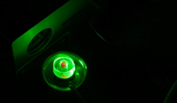 Green laser light emitted from an optical instrument in a dark laboratory setting.